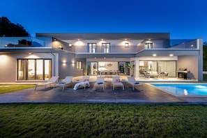Una casa moderna con piscina, mobiliario de exterior y un patio bien iluminado.