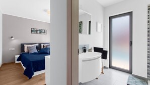Ein modernes Schlafzimmer mit Bett, Nachttisch und einem Badezimmer mit Waschbecken und Spiegel.