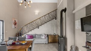 Ein moderner Wohnbereich mit einem Holzesstisch, grauen Sofas, einer Treppe mit Metallgeländer, einem Kamin und einem an der Wand montierten Flachbildfernseher.