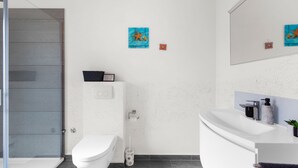 Ein modernes Badezimmer mit Duschkabine aus Glas, einer weißen Toilette und einem weißen Waschbecken mit Marmorplatte.