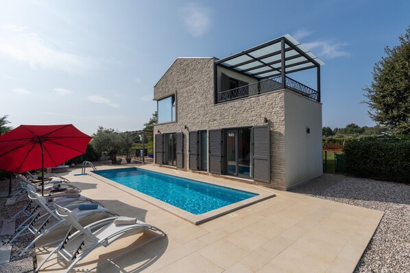 Ein modernes Haus mit Schwimmbad, Sitzgelegenheit im Freien und einem roten Sonnenschirm.
