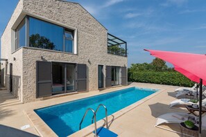 Ein modernes Haus mit Swimmingpool, großen Fenstern und einem Balkon.