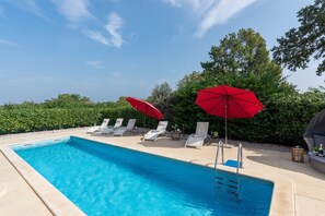 Ein Schwimmbecken mit Liegestühlen und roten Sonnenschirmen.