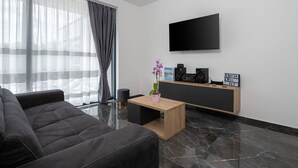 A modern living room with a dark sofa, a wooden coffee table, a flat-screen TV mounted on the wall, and a small side table with a potted orchid. - Alison Deluxe in Zupanici (Sveta Nedelja)