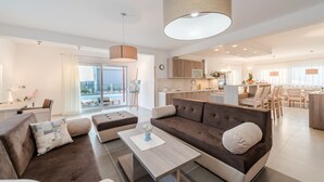 A modern living room with a sofa, ottoman, and coffee table, a dining area with chairs, and a kitchen in the background. - Dalmacija VI in Suko an (Sukosan)