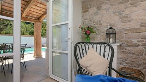 A room with a stone wall, a metal chair with a cushion, a small table, and a view of an outdoor swimming pool. - Flego in Motovun With 2 Bedrooms and 1 Bathrooms (Motovun)