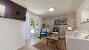 A living room with a stone wall, a flat-screen TV, a sofa, a coffee table, and a chair. - Flego in Motovun With 2 Bedrooms and 1 Bathrooms (Motovun)
