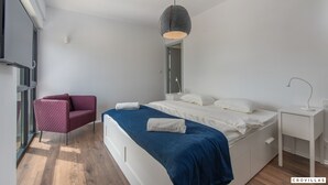 Een moderne slaapkamer met een bed, een stoel, een nachtkastje en een hanglamp.