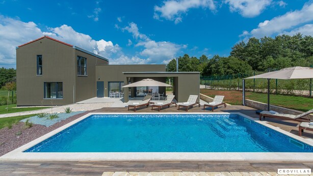 Een modern huis met zwembad, buitenmeubilair en een tuin.