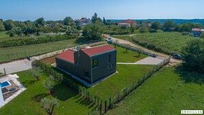 Een modern huis met twee verdiepingen, voorzien van een rood dak, omgeven door een verzorgd gazon en een omheinde tuin.