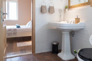 A bathroom with a white sink, toilet, and a window with a view of a bedroom.