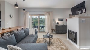 Una sala de estar moderna con un sofá, una mesa de comedor, una chimenea y un televisor montado en la pared.