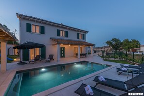 Una casa de dues plantes amb piscina, mobiliari exterior i un porxo cobert.