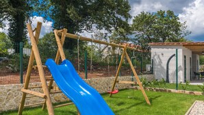Un parque infantil con un tobogán azul, columpios y un pequeño edificio.