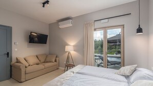 Una habitación de hotel moderna con sofá, cama, televisión, aire acondicionado, lámpara y vistas a una piscina al aire libre.