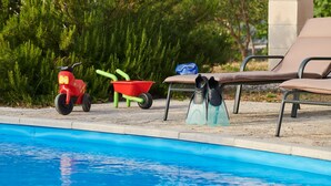 A poolside area with a pool, lounge chairs, a red toy car, a green wheelbarrow, and a pair of blue water shoes. - Stella Hvar in Rudina Hvar (Stari Grad)