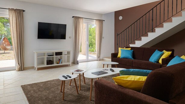 A modern living room with a brown sofa, white coffee table, and a TV mounted on the wall. - Stella Hvar in Rudina Hvar (Stari Grad)