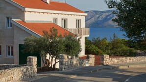 A two-story building with a red-tiled roof, stone walls, and a balcony overlooking a body of water and hills. - Stella Hvar in Rudina Hvar (Stari Grad)