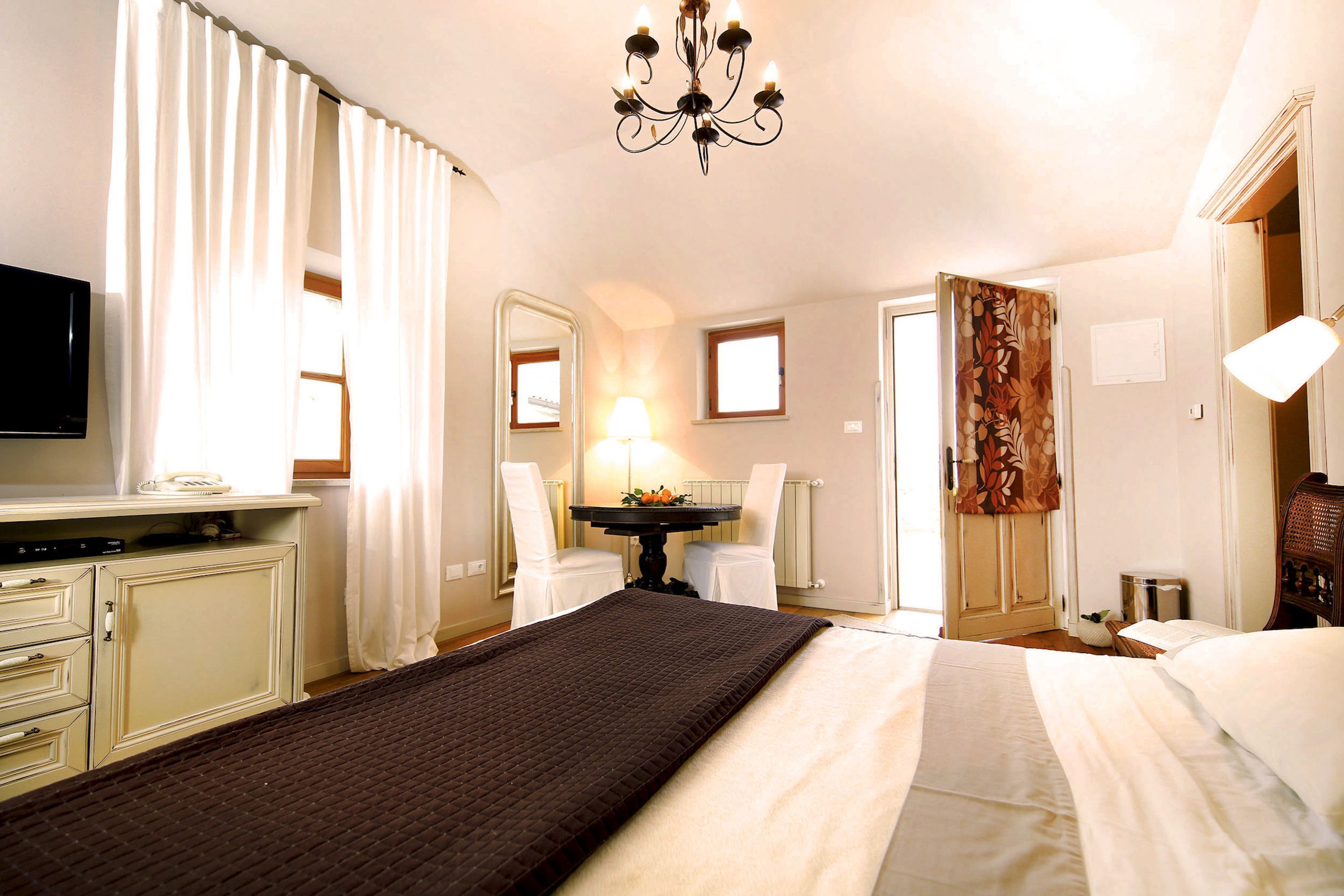 Ein Hotelzimmer mit einem Bett, einem Schreibtisch mit Fernseher, einem Sessel, einem Tisch mit Lampe und einem Kleiderschrank.
