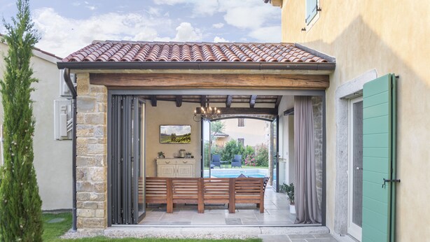 A covered outdoor seating area with stone walls, a wooden bench, and a view of a swimming pool. - Benvenuti in Motovun (Motovun)
