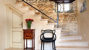 A staircase with stone walls and a wrought iron railing, a wooden side table with a vase of red flowers, and a black chair. - Benvenuti in Motovun (Motovun)