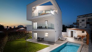 Une maison moderne à plusieurs étages, dotée d’une piscine, d’un espace extérieur aménagé et offrant une vue sur un ciel nocturne dégagé.