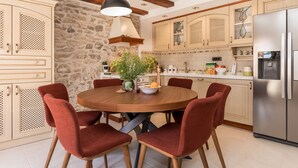 A kitchen with a round wooden table, red chairs, a stainless steel refrigerator, and stone wall features. - Josipovi Dvori in Skradin (Skradin)