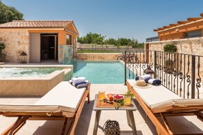 A poolside area with lounge chairs, a table with drinks and fruit, and a view of a swimming pool.