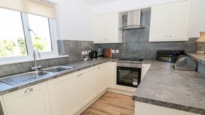 A modern kitchen with white cabinets, a built-in oven, a microwave, and a large window.
