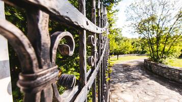 A wrought iron gate with intricate designs, leading to a stone pathway surrounded by greenery.