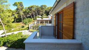 A modern building with a wooden door, a stone wall, and a view of a lush green landscape. - Bianco in Grohote Rogac Olta (Solta)