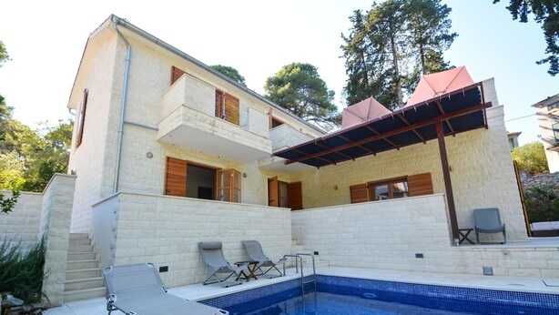 A two-story building with a swimming pool, outdoor seating, and a covered patio area. - Bianco in Grohote Rogac Olta (Solta)