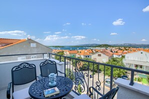 A balcony with a table and chairs, overlooking a coastal town with red-roofed buildings and a clear blue sky. - Kos in Murter With 11 Bedrooms and 6 Bathrooms (Murter-Kornati)