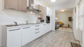 A modern kitchen with white cabinets, a stainless steel sink, and a microwave. There is a dining area with a sofa and a small table. - Amia in Pula With 3 Bedrooms and 2 Bathrooms (Pula)