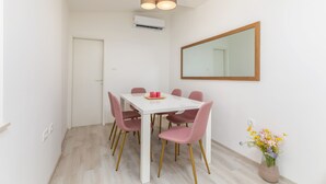 A dining area with a white table and pink chairs, a mirror on the wall, and a vase with flowers on the floor. - Amia in Pula With 3 Bedrooms and 2 Bathrooms (Pula)