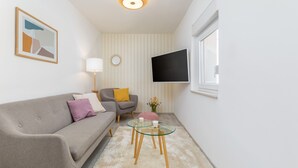 A modern living room with a sofa, a glass coffee table, a lamp, a TV mounted on the wall, and a window. - Amia in Pula With 3 Bedrooms and 2 Bathrooms (Pula)