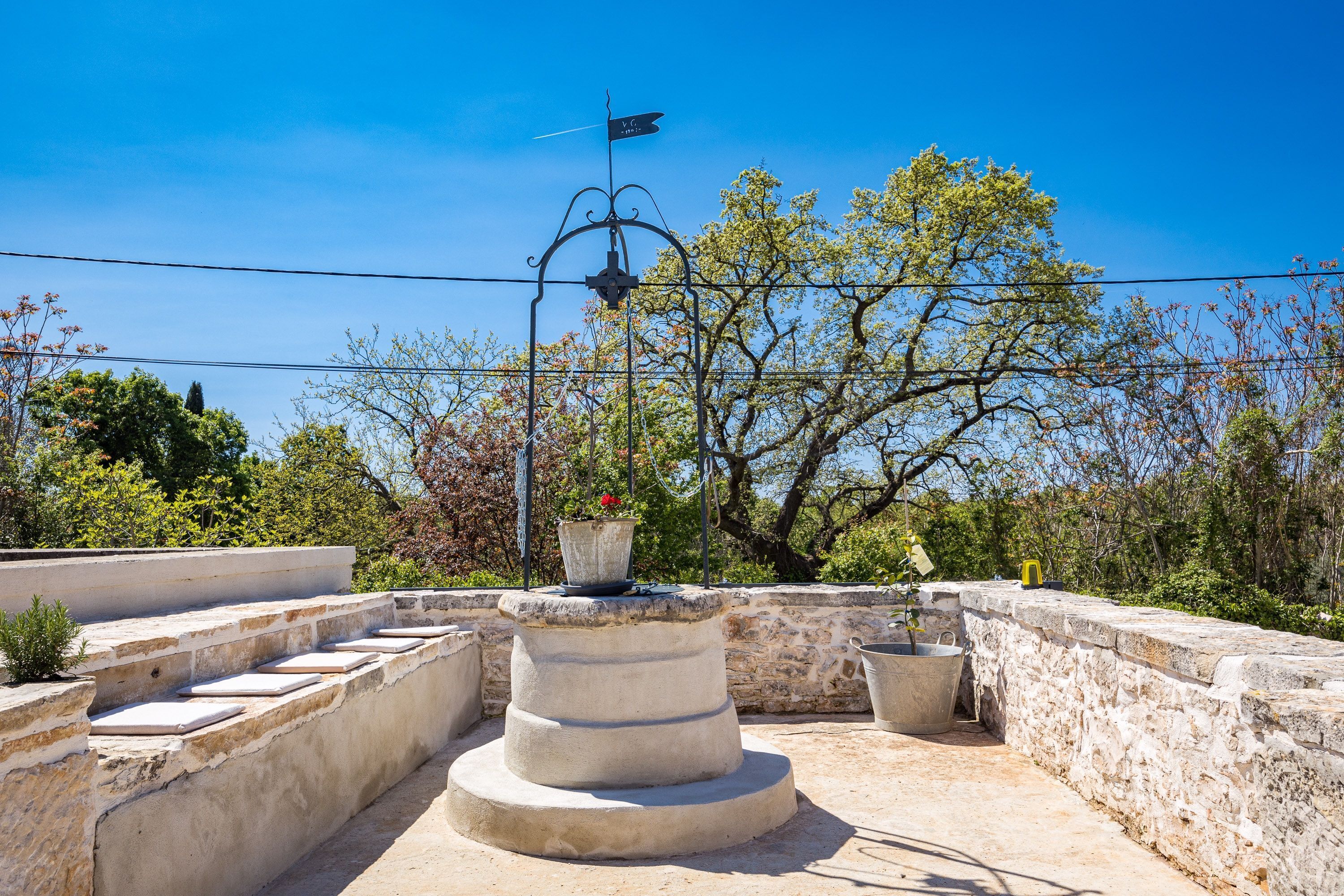 Una terraza en la azotea con un muro de piedra, un veleta y plantas en macetas.