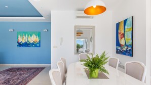 Un comedor moderno con una mesa blanca, sillas color beige, un centro de mesa con planta verde y obras de arte en las paredes.