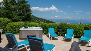Una terraza con sillones de descanso y bañera de hidromasaje, con vistas a un paisaje de colinas y una ciudad distante.