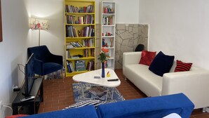 Een woonkamer met een witte bank, een blauwe fauteuil en een geel boekenkast.