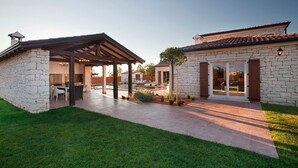 Una casa in pietra con un patio, una zona relax all'aperto coperta e un piccolo albero.