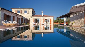 Un edificio in pietra con una piscina di fronte, caratterizzato da un ingresso centrale e un patio con posti a sedere all'aperto.