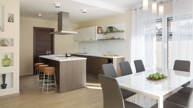 Una cocina moderna con una isla central, taburetes de bar y un comedor con mesa y sillas.