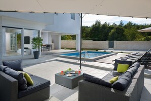 Uma área externa moderna com piscina, móveis de jardim e um alpendre envidraçado.