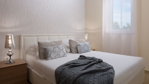 Una cama bien hecha con cabecera blanca, dos lámparas de noche y una ventana con cortinas.