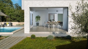Una casa moderna con piscina, un patio con mobiliario exterior y un jardín.