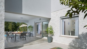 Un patio moderno al aire libre con una mesa y sillas de comedor, una planta en maceta y vista al interior a través de puertas de cristal.
