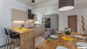 Una cocina moderna con una isla de madera, sillas negras y una mesa de comedor preparada para seis personas, con platos, vasos y un jarrón de flores.