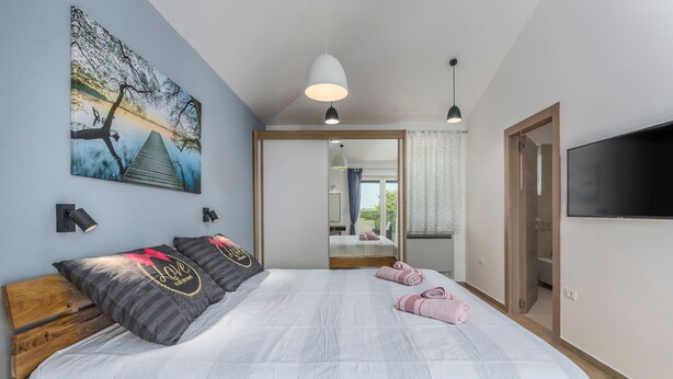 Un dormitorio con una cama grande, un cuadro de un puente, un televisor y una puerta de madera.