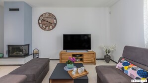 Una sala de estar moderna con un televisor de pantalla plana, un mueble de entretenimiento de madera, dos sofás, una mesa de centro con una bandeja y un reloj decorativo.